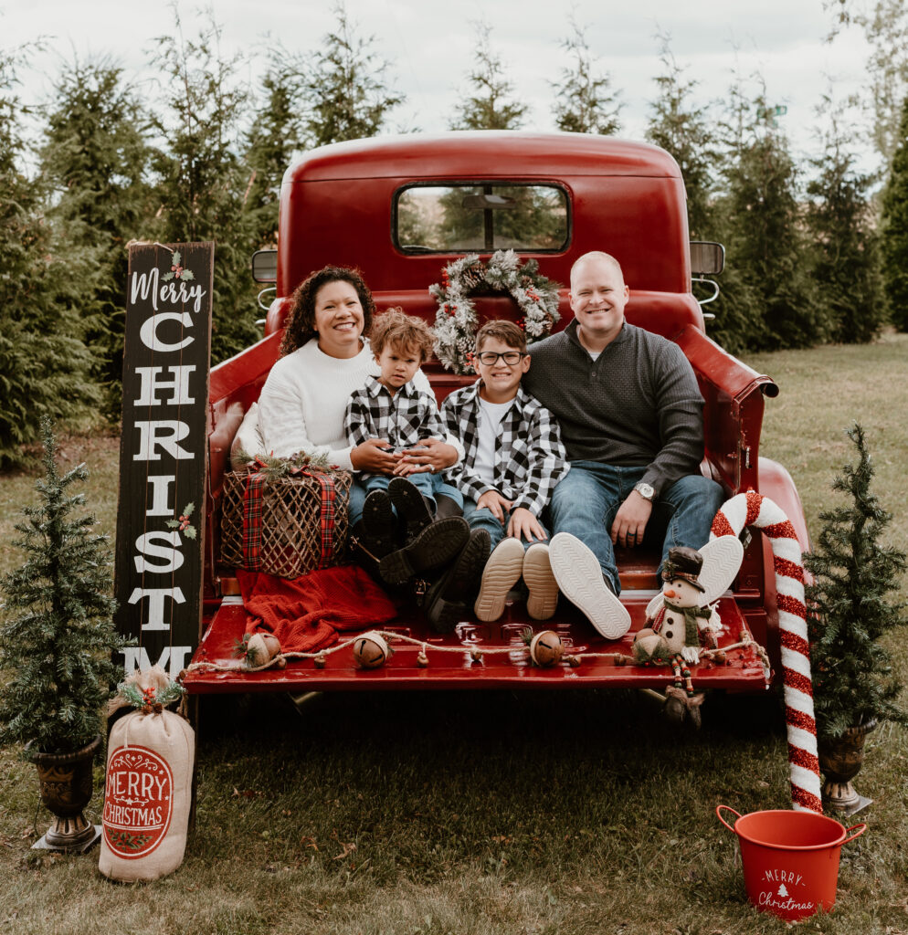 family posing on the bed of a red pickup truck for Christmas tree farm photos