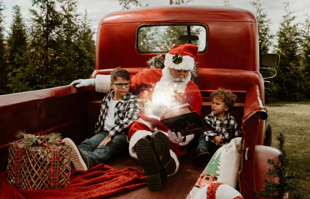 santa and children reading a book on the bed of a red pickup truck 